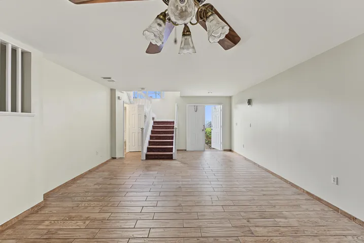 Interior space featuring wood-finish tile flooring, a multi-bulb ceiling fan, and a staircase with carpeted treads