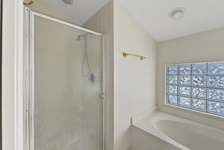 Shower with a glass enclosure, soaking tub, and glass block window