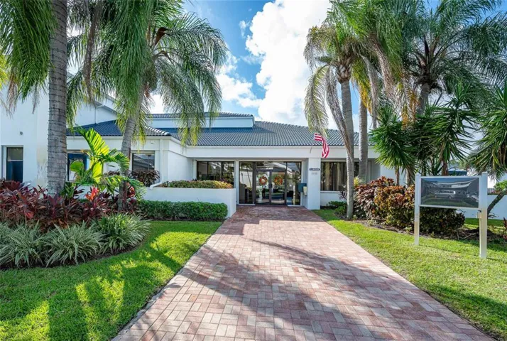 Exterior facade featuring a tile roof, glass-paneled double entry doors, brick paver walkway, and mature palm trees