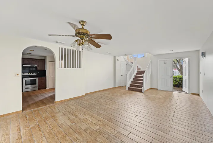 Interior space featuring wood-finish tile flooring, a prominent arched entryway, a built-in staircase with white railings, a ceiling fan with integrated lighting, and dual glass-panel entry doors