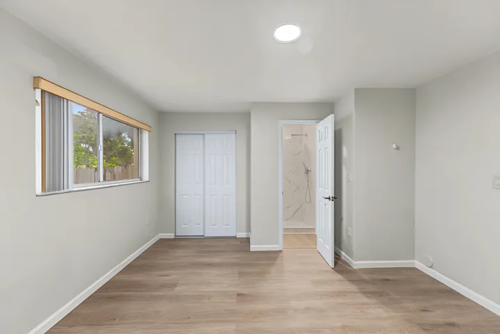Neutral-toned interior featuring wood-finish flooring, a horizontal sliding window, dual-paneled closet doors, and recessed ceiling lighting