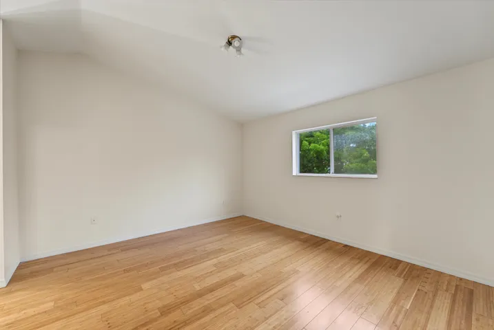 Vaulted ceiling featuring wood-finish flooring and a single-pane window