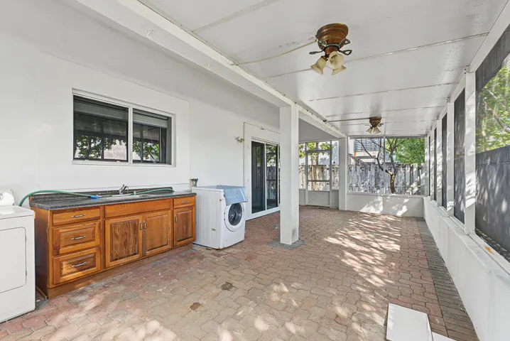 Covered screened-in patio featuring brick paver flooring, built-in wooden cabinetry with a sink, dual ceiling fans, and sliding glass entry​​‌​​​​‌​​‌‌​‌‌​​​‌‌​‌​‌​‌​​​‌​​ doors