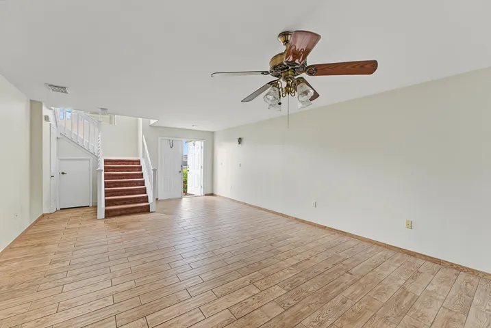 Open-concept interior featuring wood-finish flooring, a ceiling fan with integrated lighting, and a staircase with white balusters