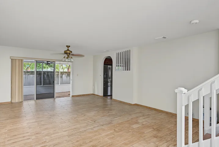 Open interior space featuring wood-finish flooring, a ceiling fan with integrated lighting, a sliding glass door, an arched entryway, and a white balustrade staircase