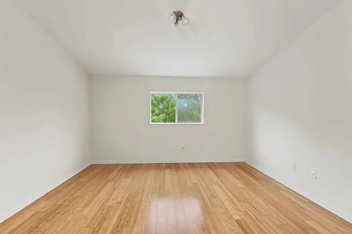 Neutral wall finishes, wood-finish flooring, and a sliding window with exterior greenery