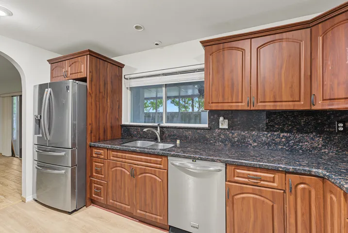 Kitchen featuring wood cabinetry, stone countertops, stainless steel refrigerator and dishwasher, and a dual-basin sink with a gooseneck faucet