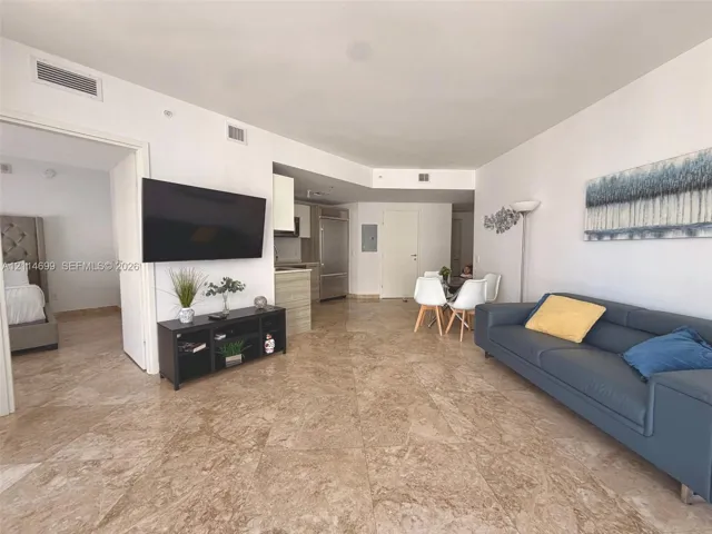 Open-concept interior featuring large-format stone tile flooring, high ceilings, built-in stainless steel refrigerator, and recessed lighting