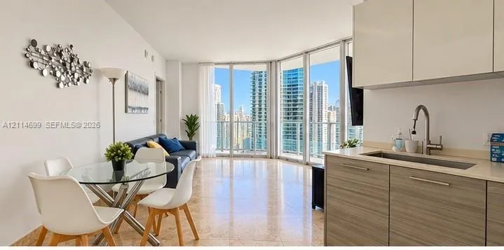 Open-concept living space featuring floor-to-ceiling windows, polished stone flooring, high-gloss upper cabinetry, and wood-finish lower kitchen cabinetry with a stainless steel undermount sink
