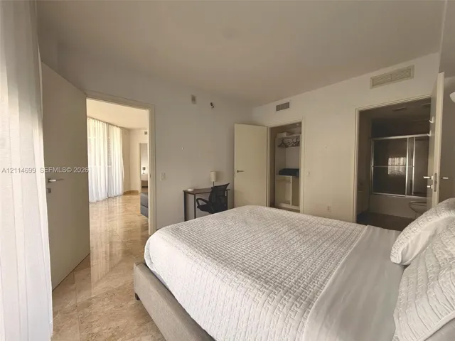 Spacious room featuring polished stone flooring, built-in closet cabinetry, and a private ensuite bathroom with a glass-enclosed shower