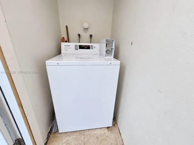 Recessed laundry area featuring a white top-load washer, coin-operated mechanism, and stone-finish tile flooring