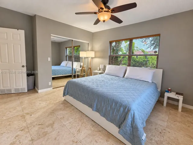 Neutral-toned interior featuring large-format stone flooring, mirrored sliding closet doors, and a ceiling-mounted light fixture with integrated fan