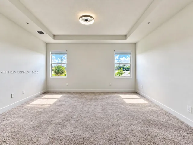 Tray ceiling, neutral carpeting, dual windows with roller shades, and integrated flush-mount ceiling lighting