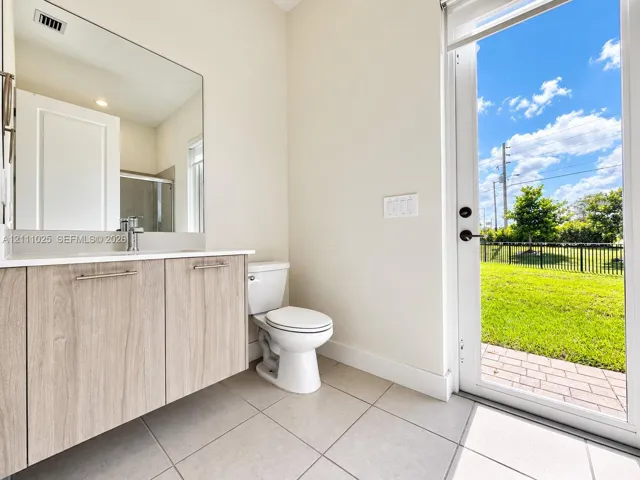 Floating vanity featuring wood-finish cabinetry, crisp countertop, large wall-mounted mirror, ceramic tile flooring, and glass-paned door providing outdoor access