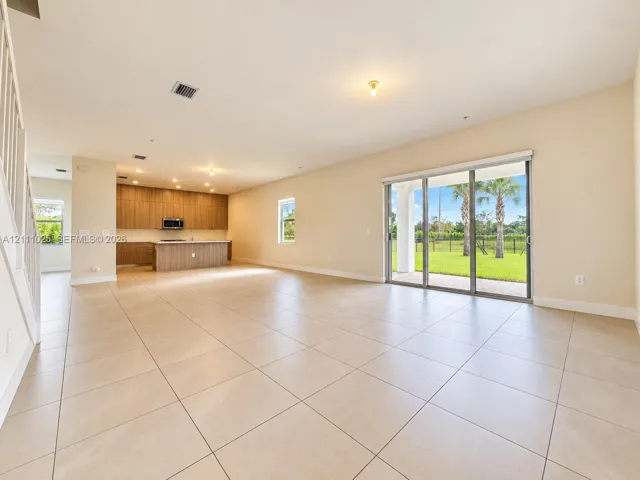 Open-concept interior featuring large-format tile flooring, wood-finish cabinetry, a central kitchen island, and sliding glass doors