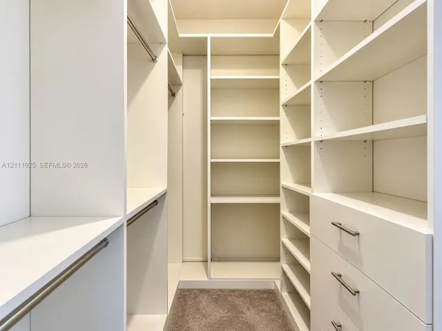 Customized walk-in closet featuring floor-to-ceiling white cabinetry, adjustable shelving, integrated garment rods, and built-in drawers with metallic hardware