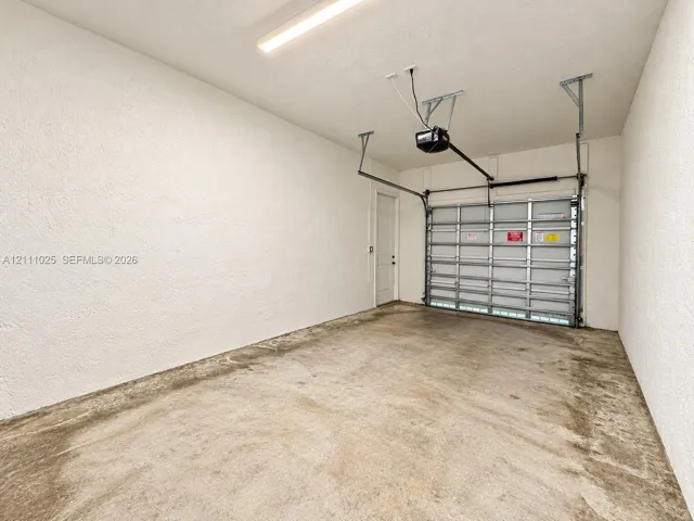 Enclosed garage featuring textured walls, concrete flooring, overhead lighting, and an automated roll-up door