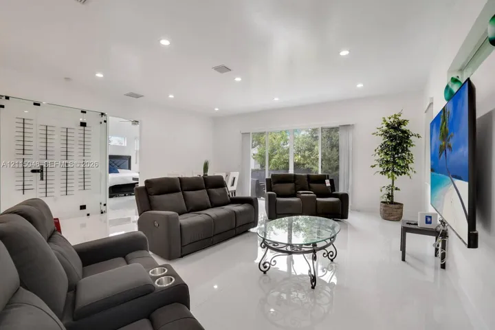 Open-concept living space featuring high-gloss tile flooring, recessed lighting, and a glass-enclosed wall wine display