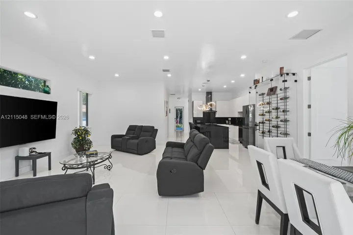 Open-concept interior featuring large-format tile flooring, recessed ceiling lighting, a built-in wall-mounted wine rack, and a kitchen island with a black countertop