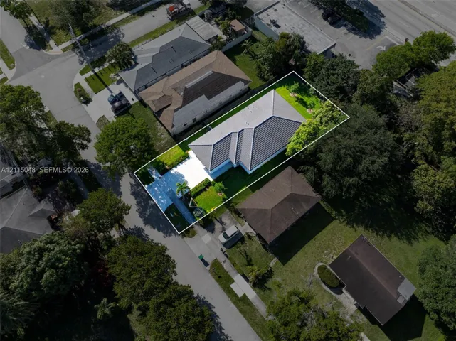Aerial view featuring a single-story residence with a concrete tile roof, paved driveway, and established lawn areas with mature trees