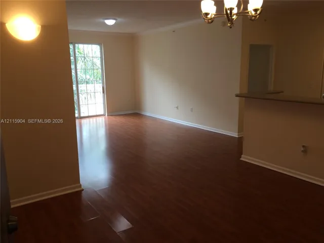 Wood-finish flooring, glass sliding doors, crown molding, tiered chandelier, and breakfast bar
