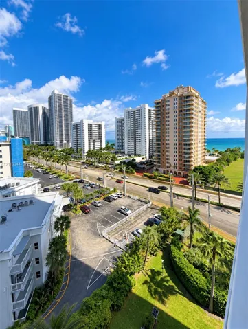 Elevated urban perspective featuring coastal water scenery, mature palm trees, multi-story high-rise architecture, and professional landscaping