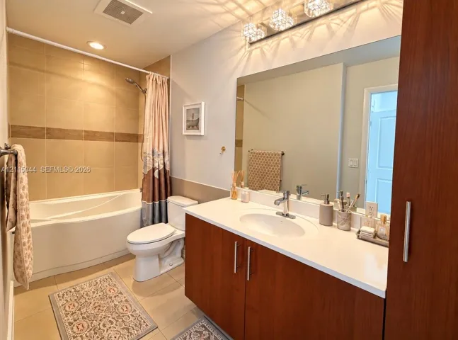 Bathroom featuring a deep soaking tub with tile surround, wood-finish vanity cabinetry, quartz countertop with an integrated oval sink, and a multi-bulb vanity light fixture