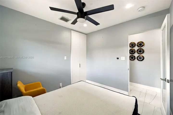 Neutral-toned interior room featuring a matte black ceiling fan, recessed lighting, white built-in cabinetry, and white tile flooring with grey veining