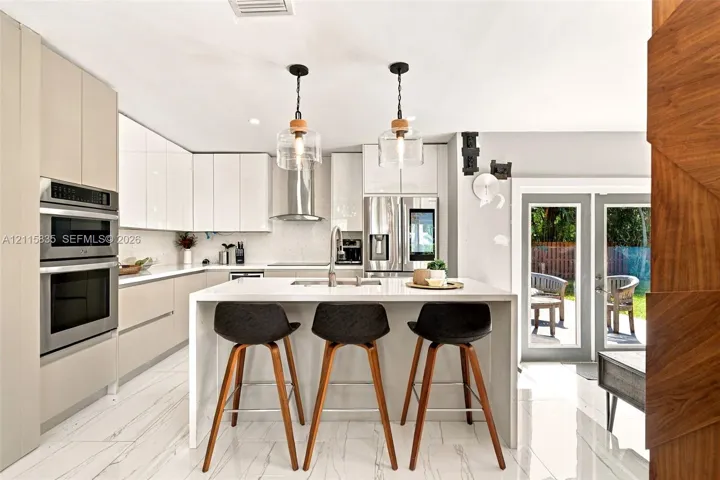 Modern kitchen featuring high-gloss cabinetry, stainless steel built-in double wall ovens, a central island with a solid-surface countertop, and glass pendant lighting