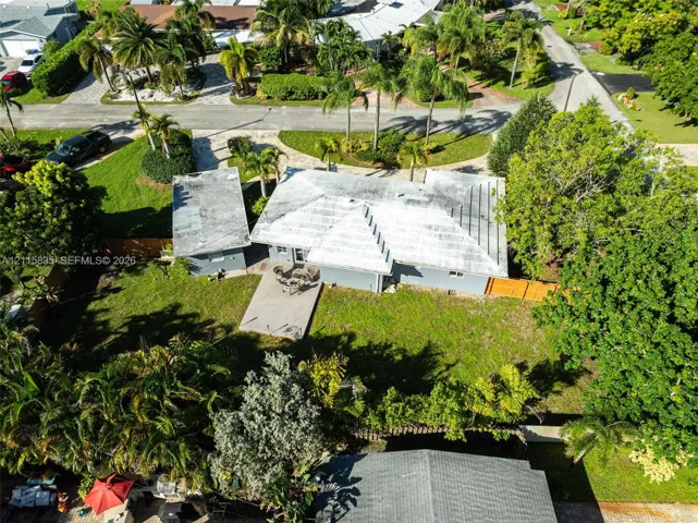 Aerial view of a detached residence featuring a concrete patio, wood-style fencing, and mature landscaping on a corner lot