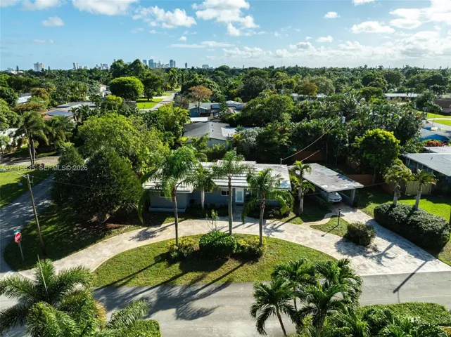 Single-story residence featuring a paved circular driveway, attached carport, mature palm landscaping, and light-toned roof shingles