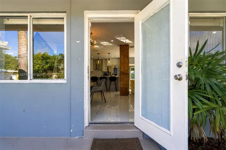 Entryway featuring a white door with integrated blinds, polished tile flooring, and a decorative wood-finished pillar