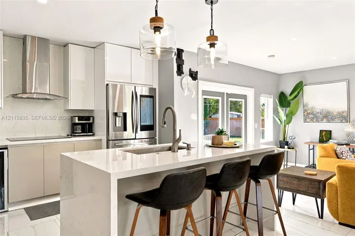 Contemporary kitchen featuring a waterfall-edge quartz island, sleek handle-less cabinetry, stainless steel appliances, a high-arc pull-down faucet, and dual glass pendant light fixtures