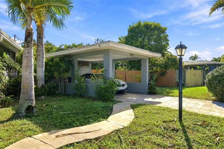 Covered carport structure with a paved stone driveway, complemented by a stone walkway, mature palm trees, and an exterior lantern-style lighting fixture
