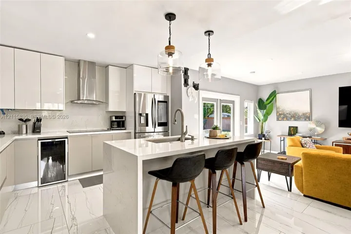 Modern kitchen featuring high-gloss cabinetry, a central island with a quartz countertop, stainless steel appliances, stone-finish tile flooring, and glass pendant lighting