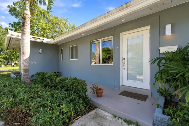 Exterior entrance featuring a painted stucco facade, white-framed windows, a glass-panel entry door, and recessed lighting