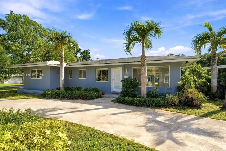 Single-story residence featuring a painted stucco exterior, low-pitch roofline, concrete driveway, and mature palm tree landscaping