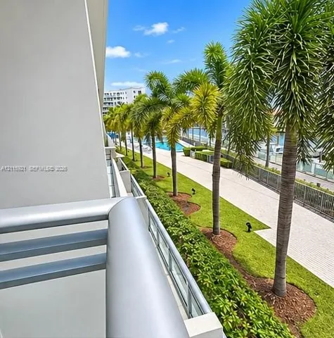 Balcony featuring metal railings, overlooking manicured landscaping, palm trees, a paved walkway, and a swimming pool