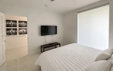 Neutral-toned interior featuring large-format tile flooring, a floor-to-ceiling window with a roller shade, and a louvered closet door