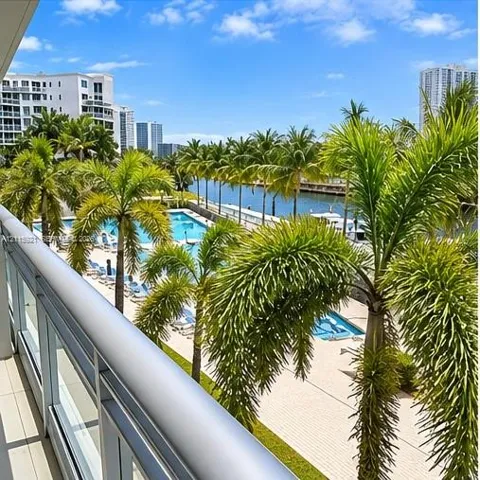 Balcony featuring a metal railing, overlooking a swimming pool, palm trees, and a waterway