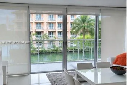 Floor-to-ceiling sliding glass doors opening to a balcony with metal railings, tile flooring, and integrated roller shades
