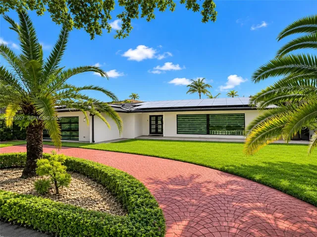 Contemporary single-story exterior featuring a red paver driveway, manicured landscaping, horizontal multi-pane windows, and rooftop solar panels