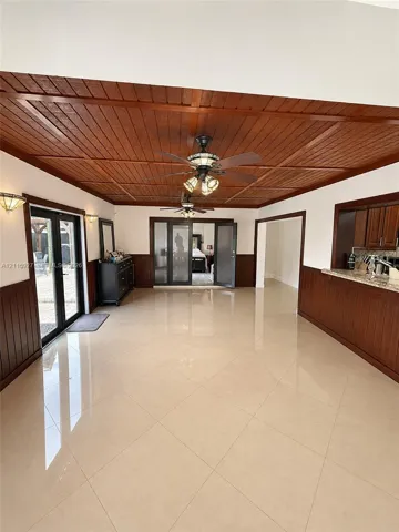 Coffered wood-plank ceiling, porcelain tile flooring, wood wainscoting, dual ceiling fans, and French doors