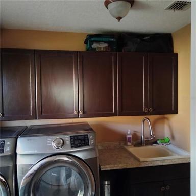 The utility room has a sink and storage cabinets and stainless steel washer and dryer