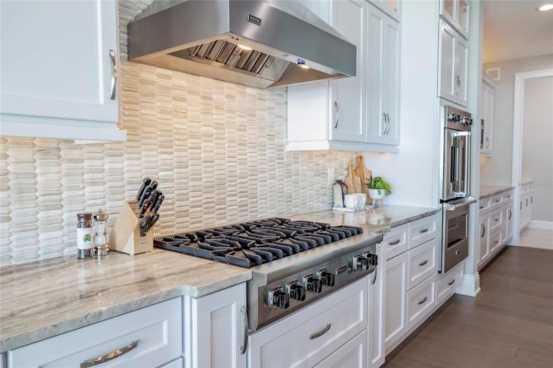 Viking gas cooktop and Viking exhaust top hood.  Further to the right of the wall ovens is a coffee center, a full laundry and a walk in pantry.