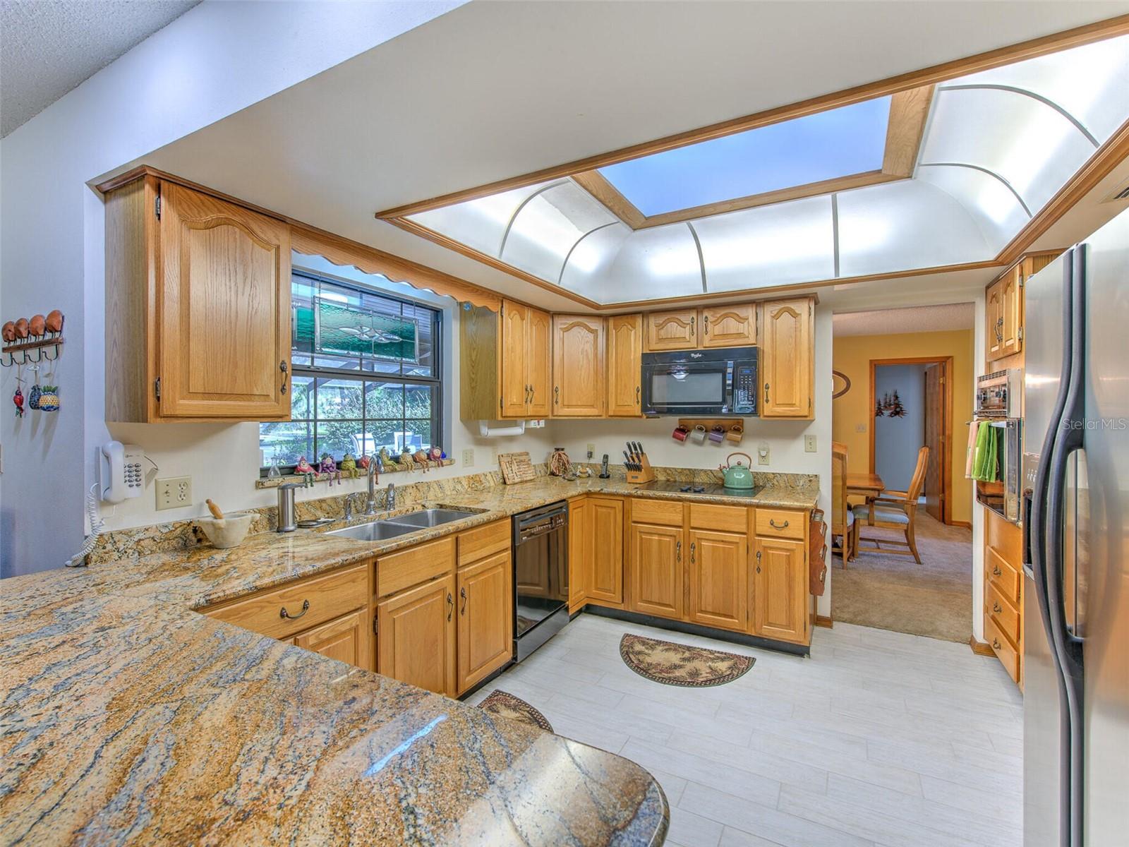 DAYTIME View of open kitchen with skylight, solid wood cabinets, granite countertops and window overlooking the lanai.