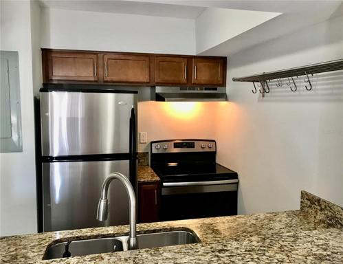 Wood cabinets, granite counters, and stainless appliances include refrigerator, range, dishwasher, and double sink with disposal. Stainless shelving and breakfast bar maximize space functionality.