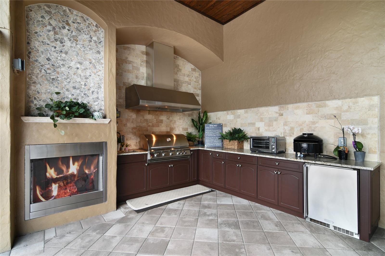 Outdoor Kitchen with Grill and vented hood, mini fridge and fireplace.