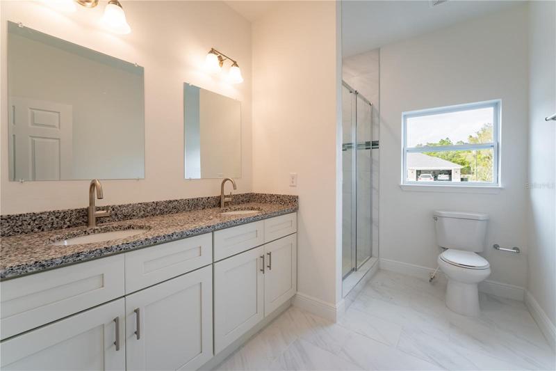 Double sink and shower stall in the primary bathroom. Granite countertop.  This is a model; the actual colors, finishes, and orientation may be different.