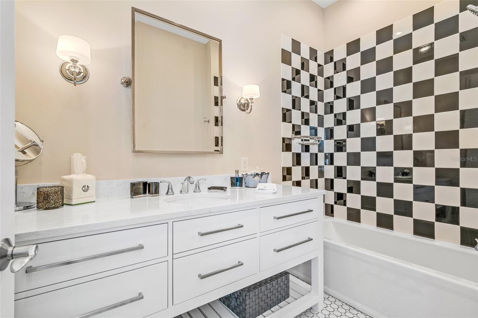 2nd floor guest bathroom. Large vanity with custom cabinetry, quartz counter, designer mirror and lighting. The checkerboard tile display in the tub/shower coordinate perfectly with the floor tiles. This bathroom offers a private water closet, as well.